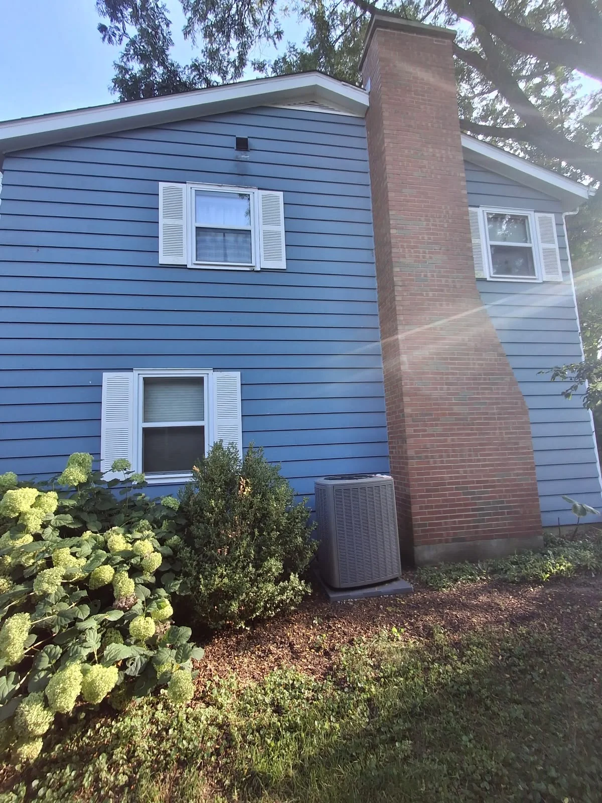 Blue house siding with white shutters and a brick chimney after painting