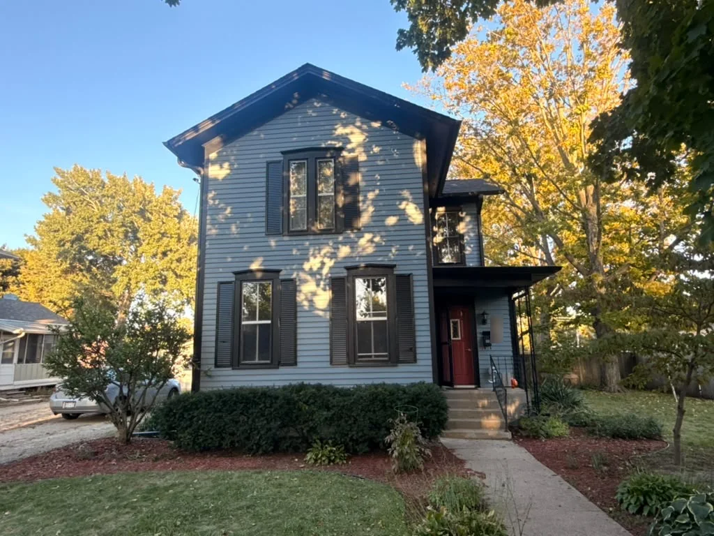 Front of a two-story house with blue-gray siding, dark shutters and trim, and a red front door