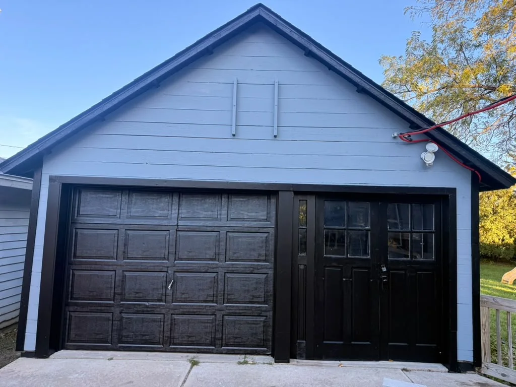 Detached garage with black doors and trim and light blue siding