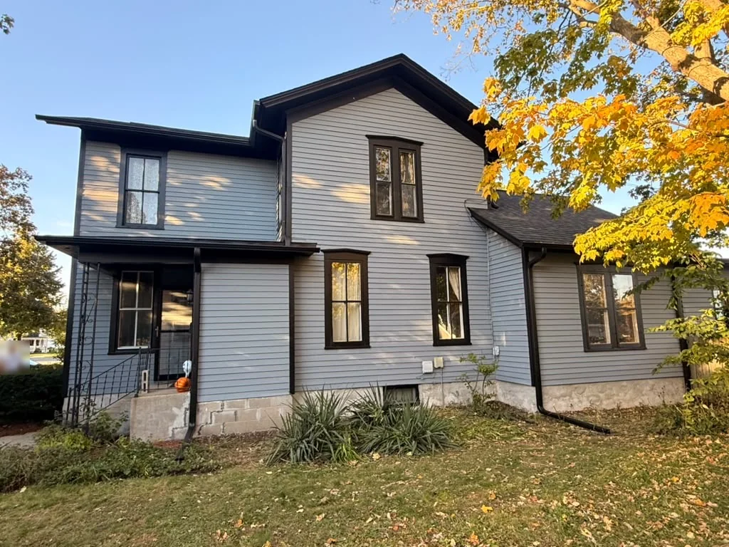Side of an older home painted gray-blue with dark brown window trim and gutters