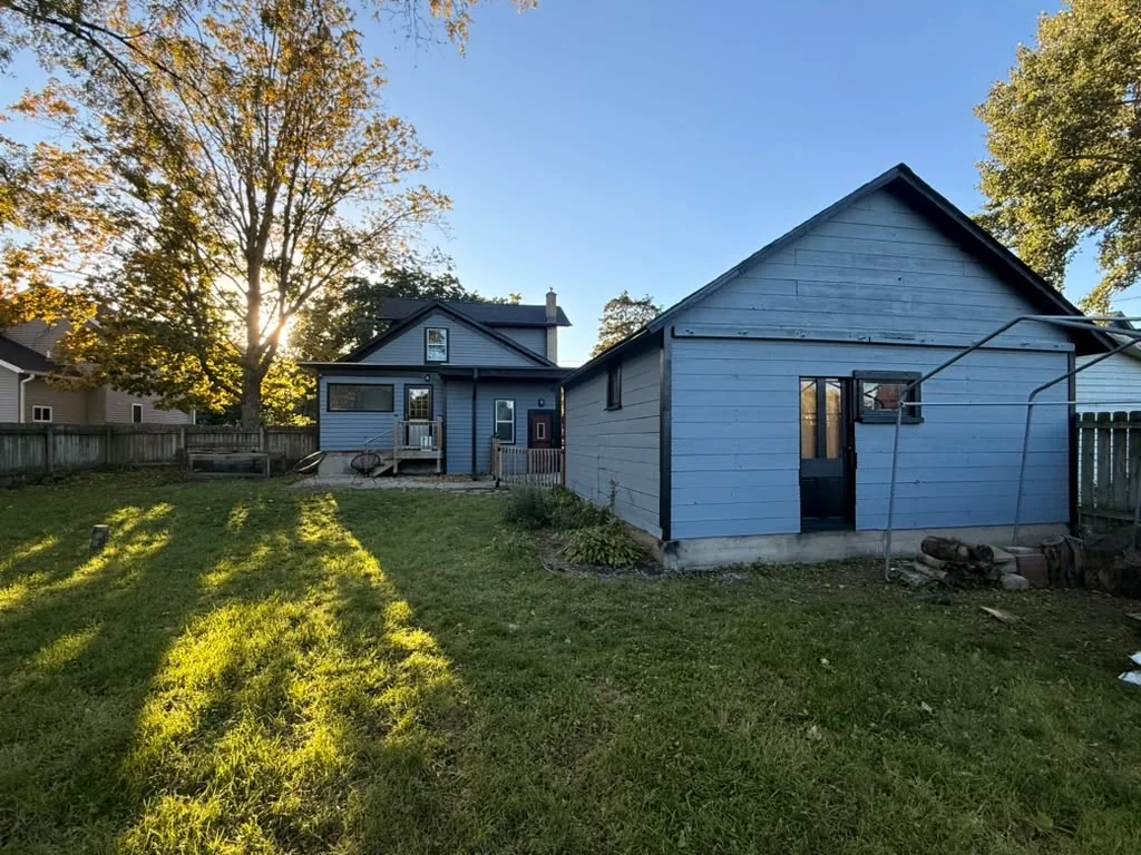 Backyard view of a house and detached garage painted blue with black trim